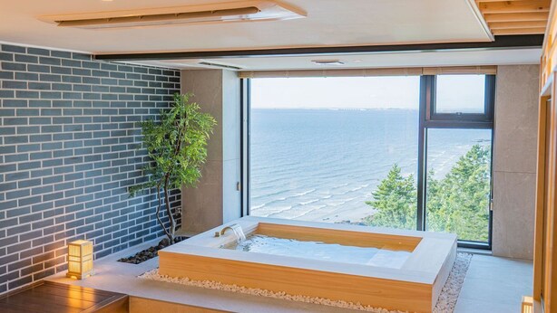 Un moderno espacio de spa con una bañera grande, una pared de ladrillo y vistas al mar.