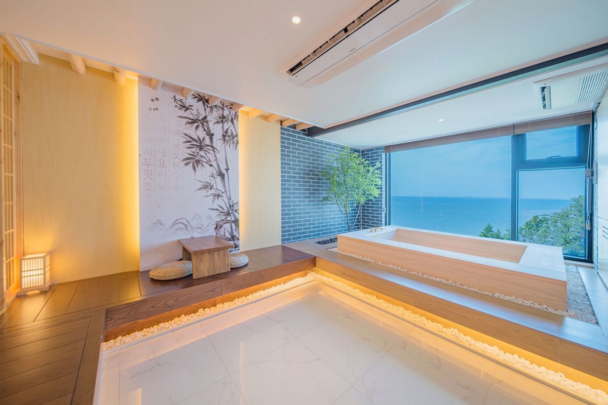 A modern spa room with a large bathtub, a wooden bench, and a view of the sea.