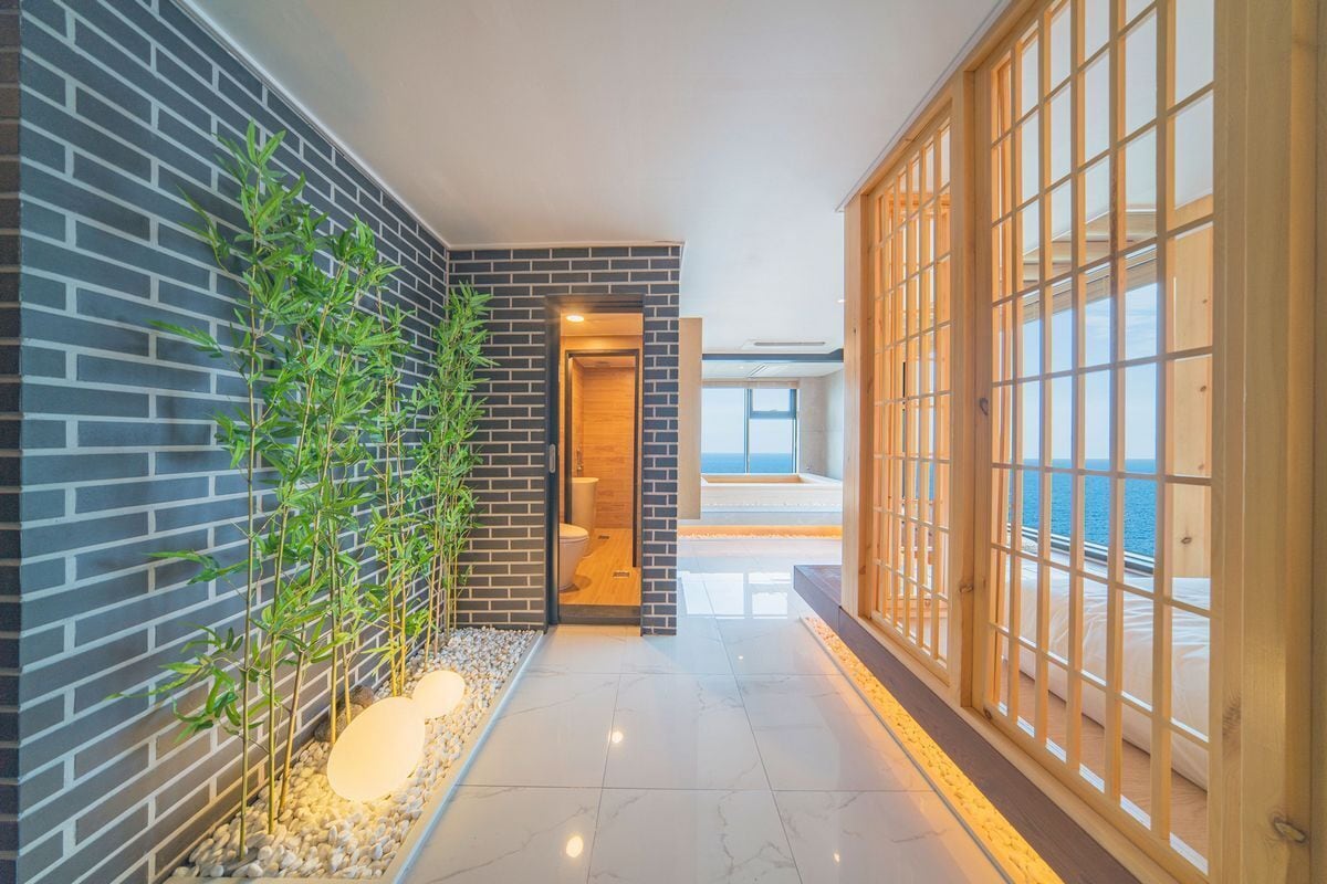 A modern hallway with a brick wall, a bamboo plant, and a wooden sliding door leading to a balcony with a view.