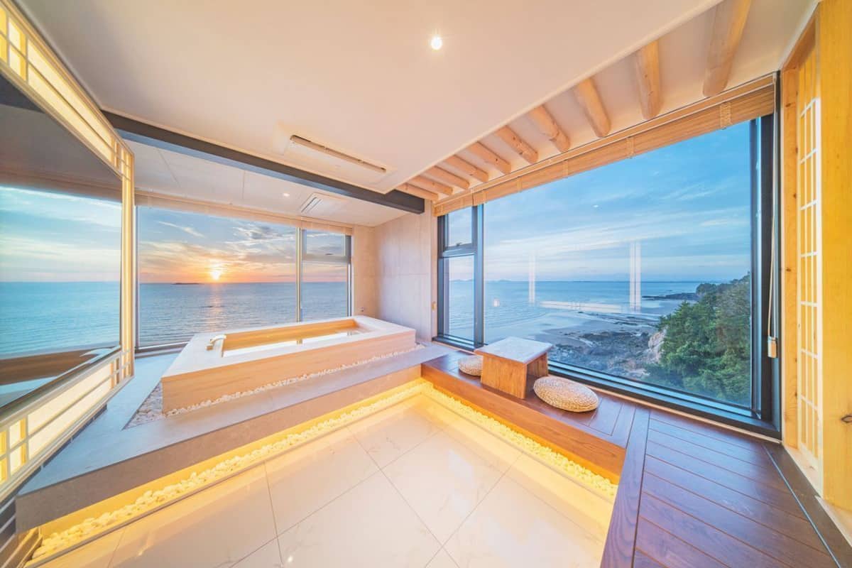 Un moderno spa con un ventanal grande que da al mar, una banca de madera y una bañera de hidromasaje integrada.