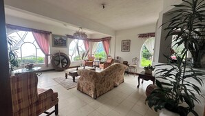 Ein geräumiges Wohnzimmer mit großem Fenster, einem runden Tisch, floralen Sofas und einer Topfpflanze.