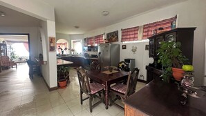 Eine geräumige Küche mit einer zentralen Kochinsel, ein Essbereich mit Holzkreisl und eine Wohnfläche mit Sofa und Fernseher.