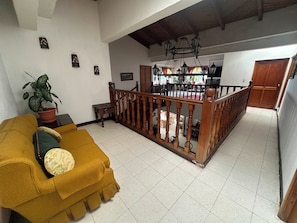 A living room with a yellow sofa, a staircase with a wooden railing, and a potted plant.