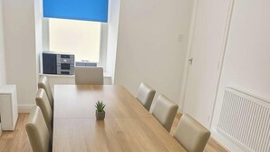 A conference room with a long wooden table, beige chairs, a small plant, and a window with a blue blind. - 5 beds/Spacious 4-Bedroom Retreat in the Heart of Churchill  with Parking (North Somerset)