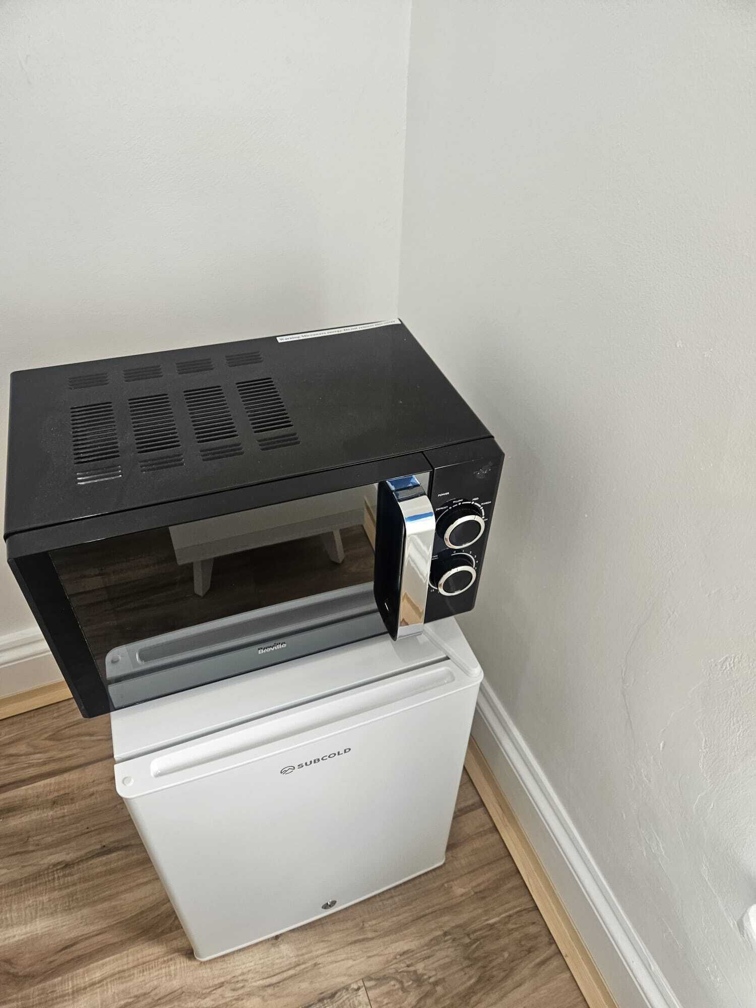 Een compact keukenhoekje met een zwarte magnetron bovenop een witte koelkast.