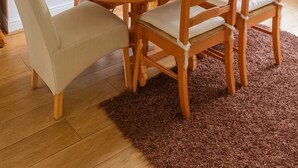 Een eetgedeelte met een ronde houten tafel, zes stoelen, een potplant en een spiegel boven de tafel.