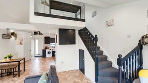 A spacious living area with a herringbone floor, a sofa, a dining table, and a kitchen in the background. - Chic Urban Haven with Double Bed House (Bristol City)