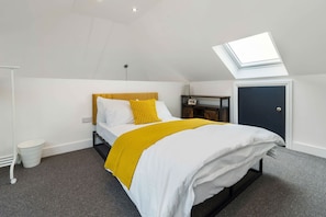 A bedroom with a bed, a skylight, a white wall, a door, and a small table with a lamp. - Chic Urban Haven with Double Bed House (Bristol City)
