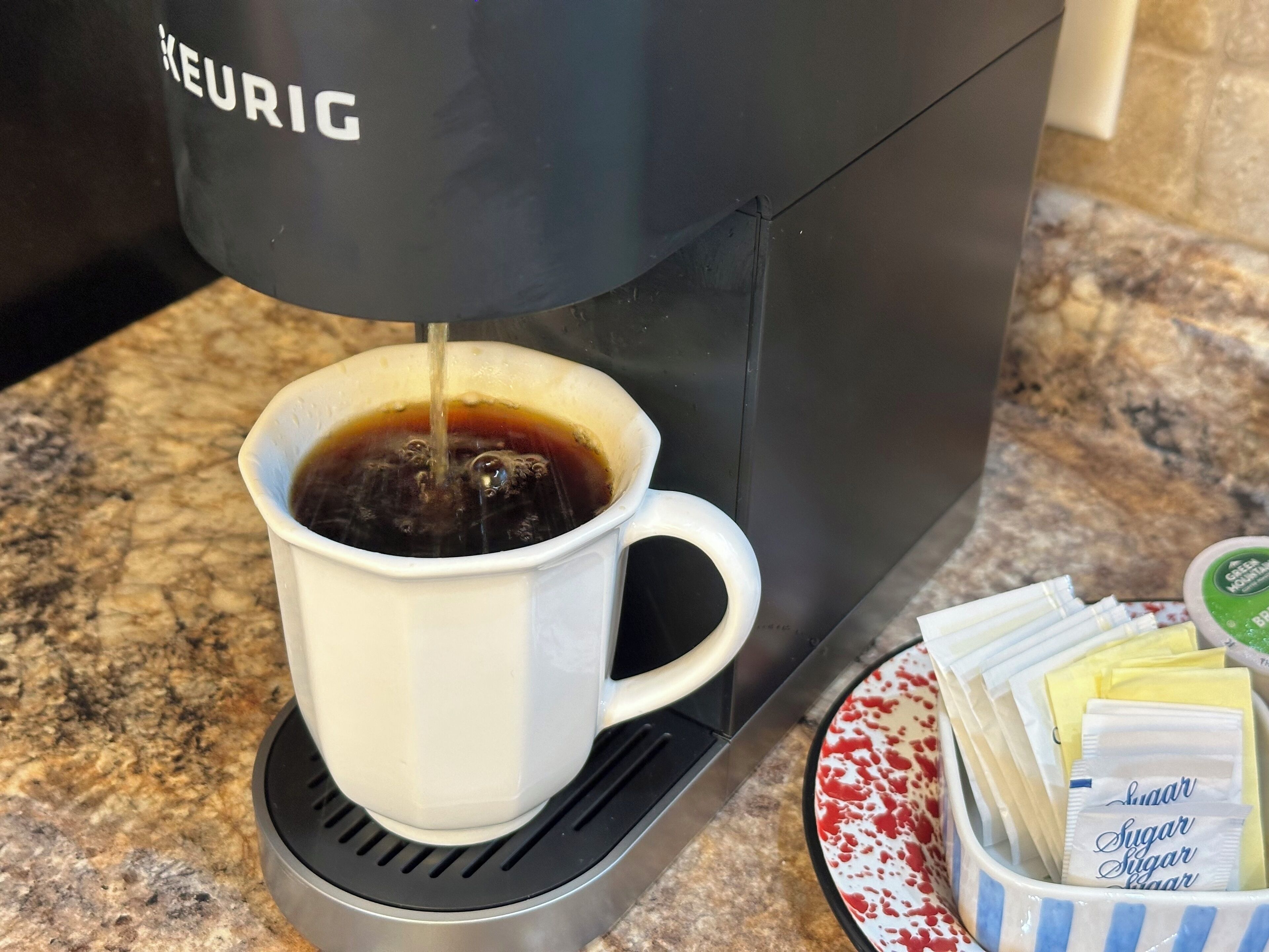 Une machine à café de la marque KEURIG verse du café dans une tasse blanche.