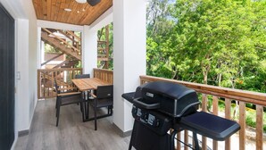 A balcony with a wooden deck, a barbecue grill, and a dining area with a table and chairs.