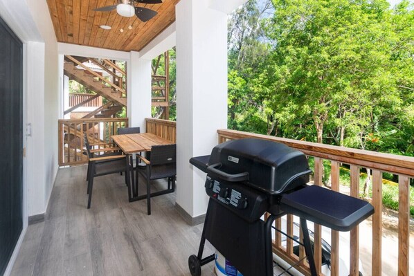 A balcony with a wooden deck, a barbecue grill, and a dining area with a table and chairs.