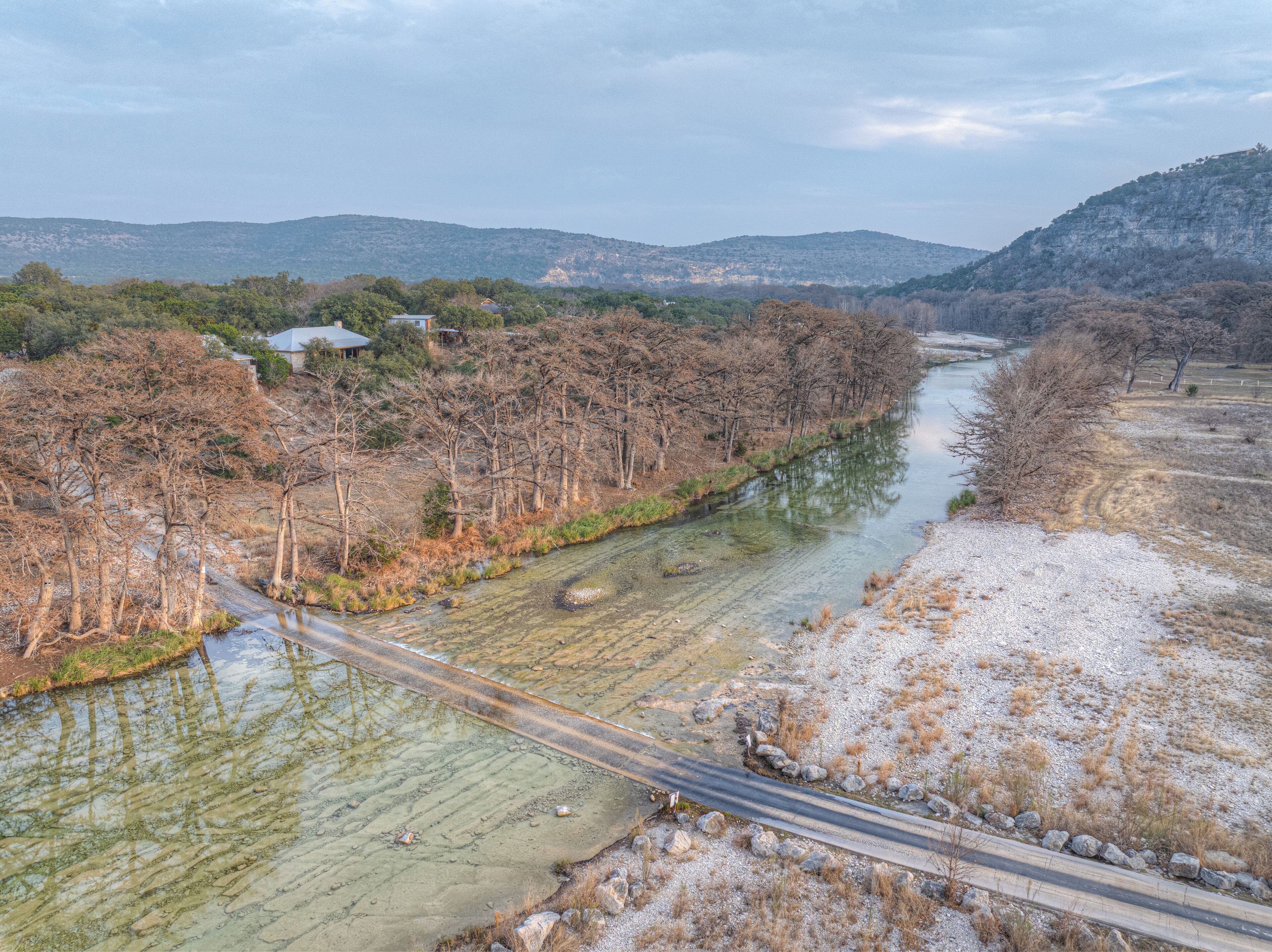 A river with a road alongside it, surrounded by trees and hills in the background.