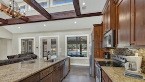 A spacious kitchen with granite countertops, wooden cabinets, and a large island. It features a dishwasher, oven, and coffee maker. - 5 Bed Room House with Pool, Pickleball, Basketball, Sand Volleyball on Hole #1  (Concan)
