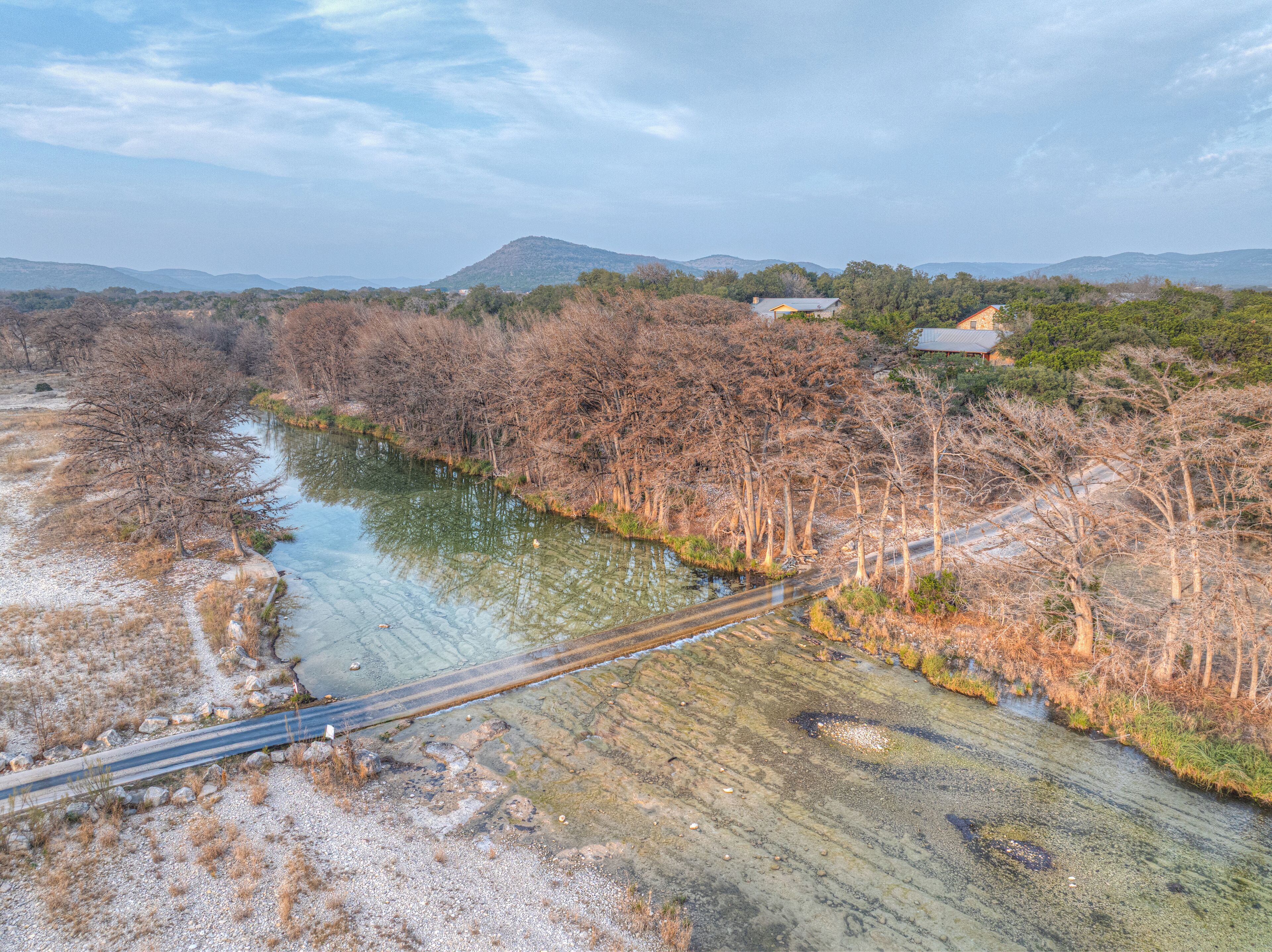 A river with a bridge and trees, surrounded by hills.