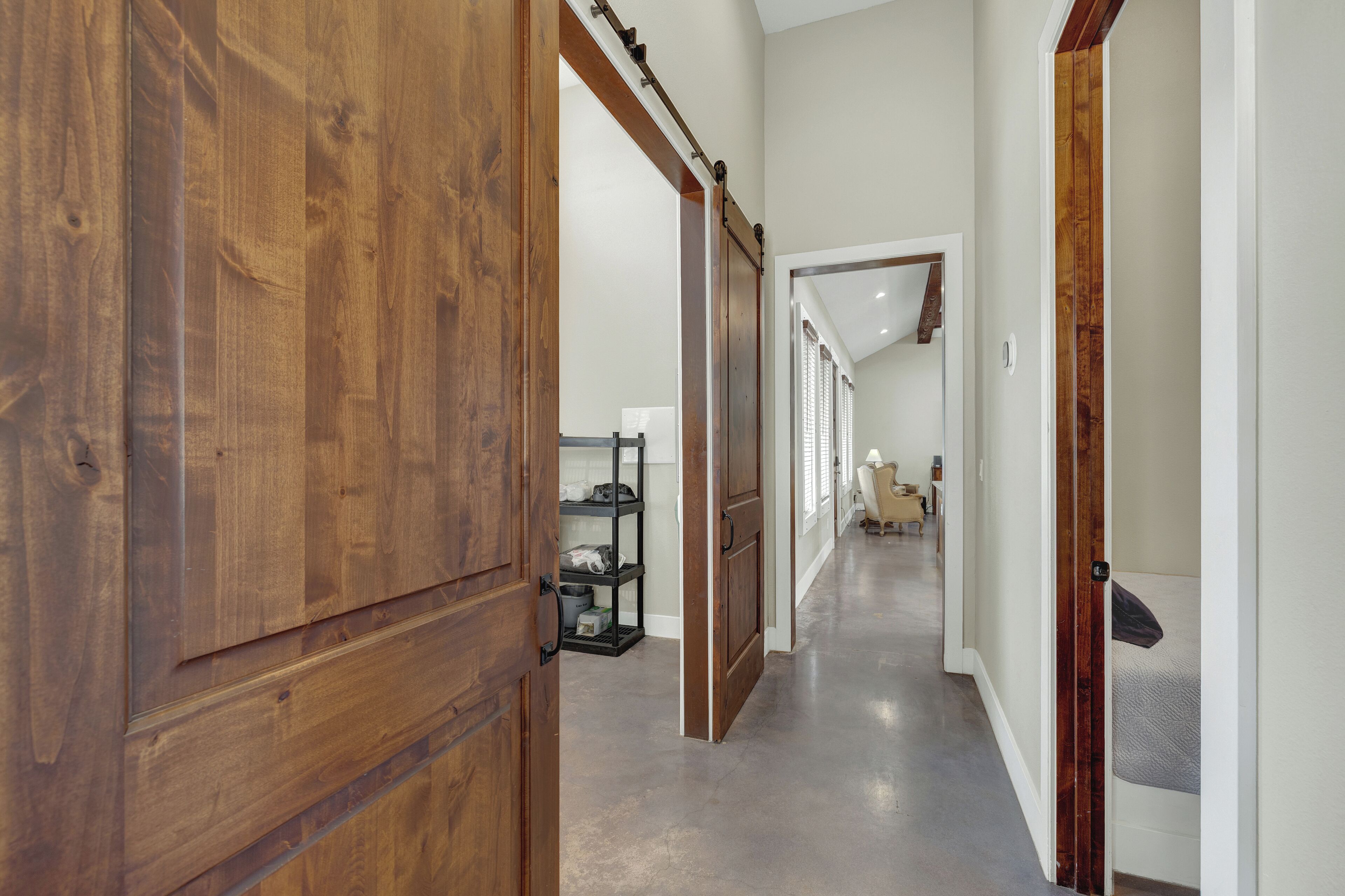 A hallway with wooden doors, a metal shelf unit, and a bed in the distance.