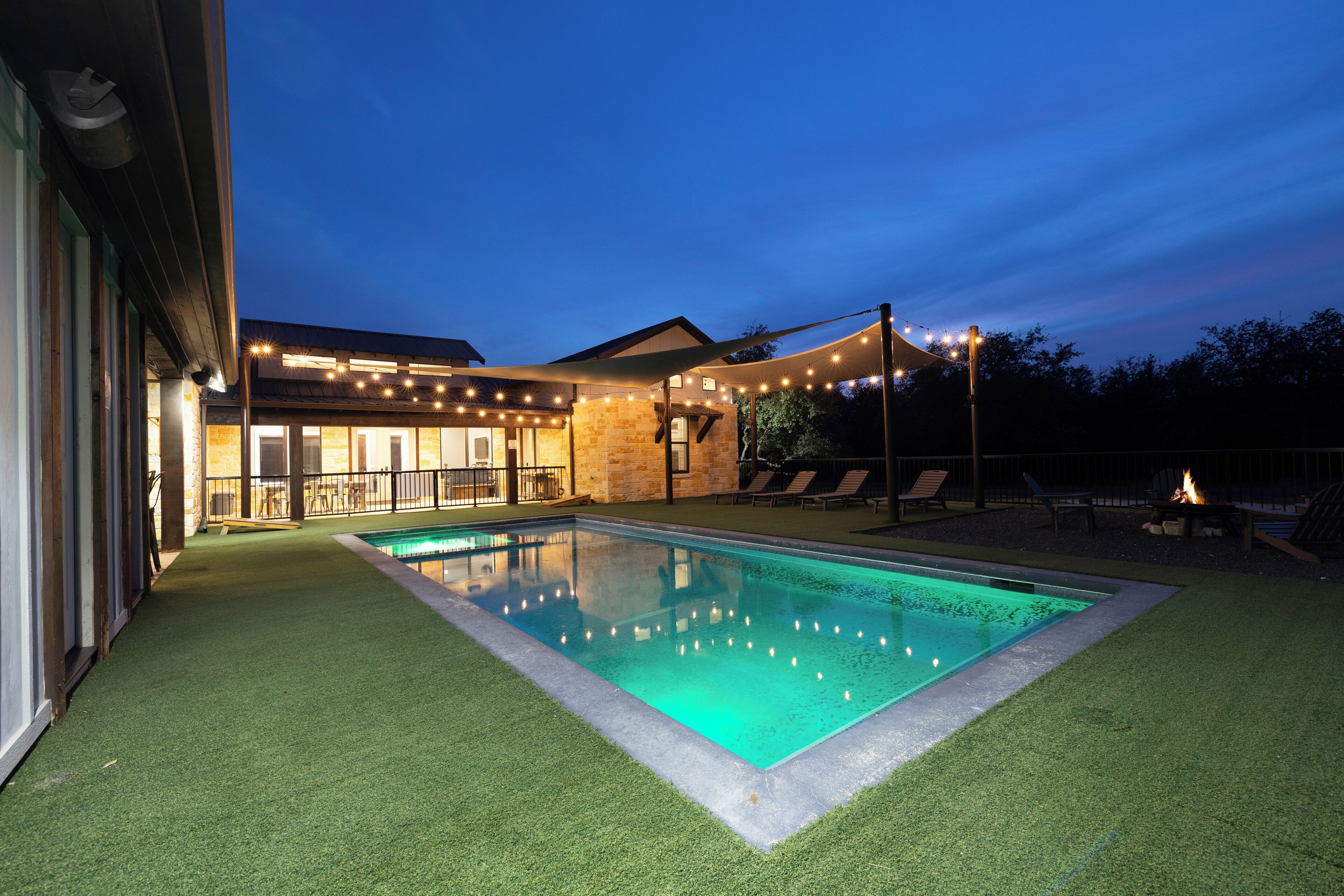 A swimming pool with a surrounding deck, a covered seating area, and string lights.