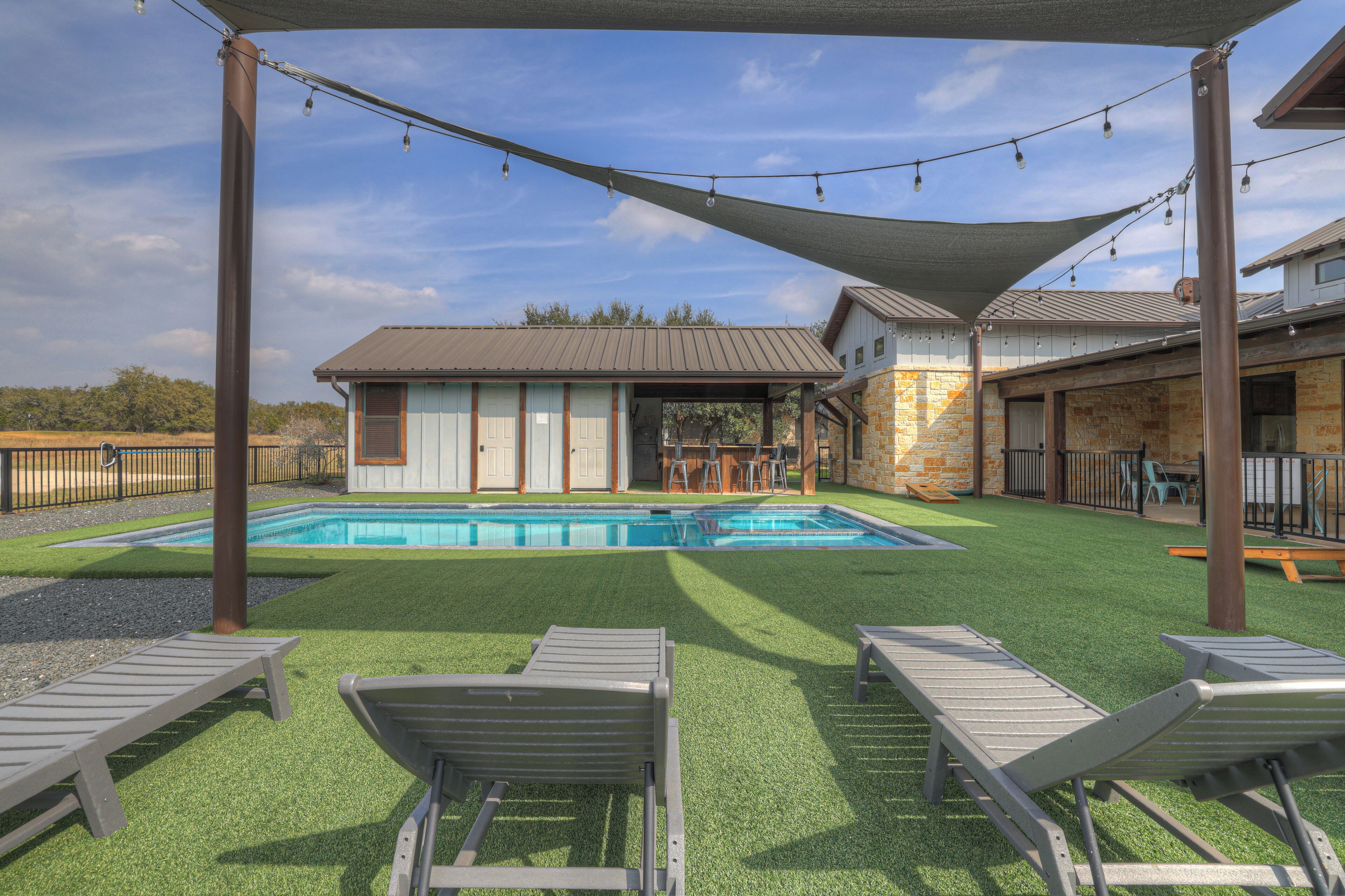 A backyard with a swimming pool, artificial grass, and lounge chairs.
