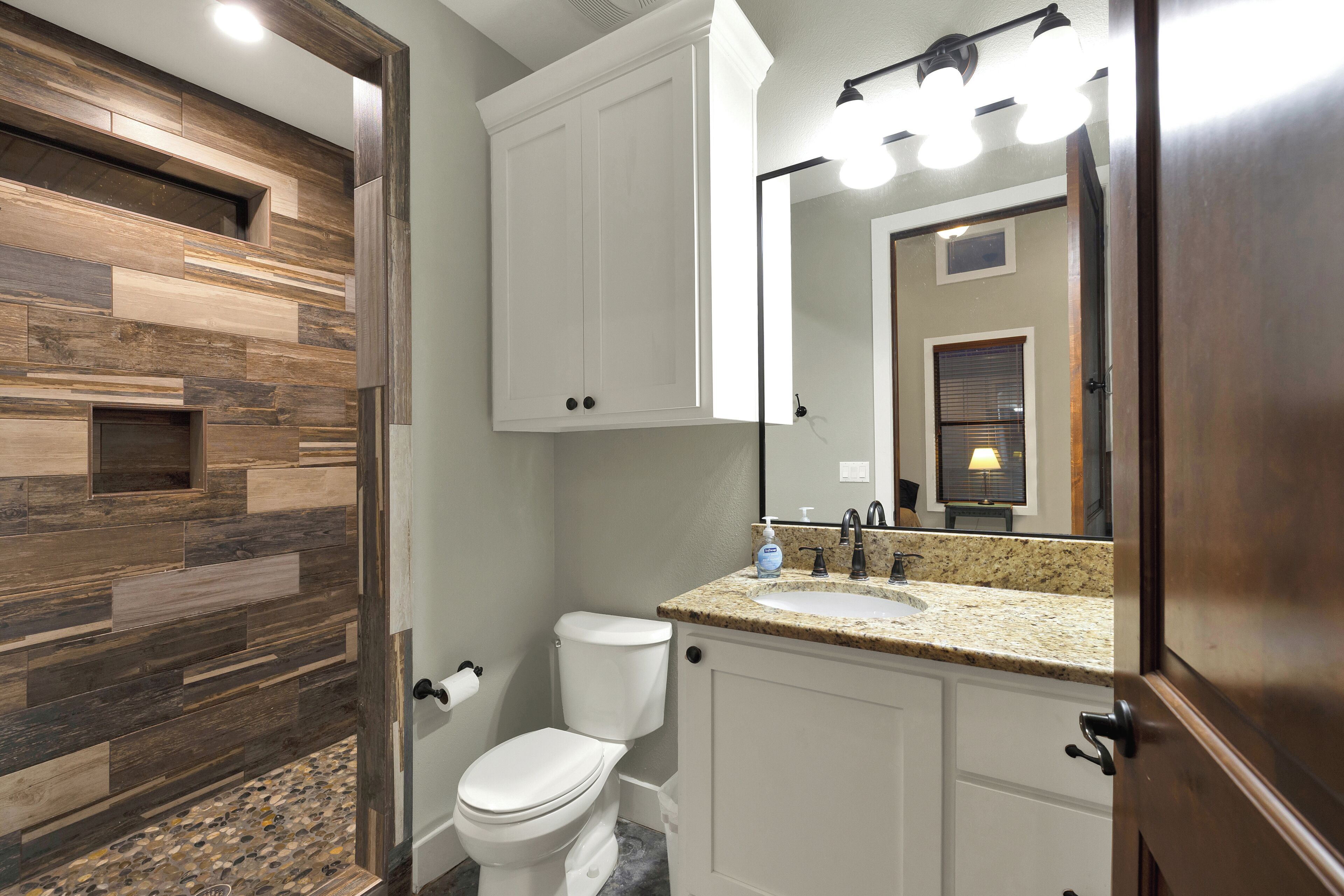 A bathroom with a wooden wall design, a white toilet, a sink with a mirror above it, and a door with a light fixture.