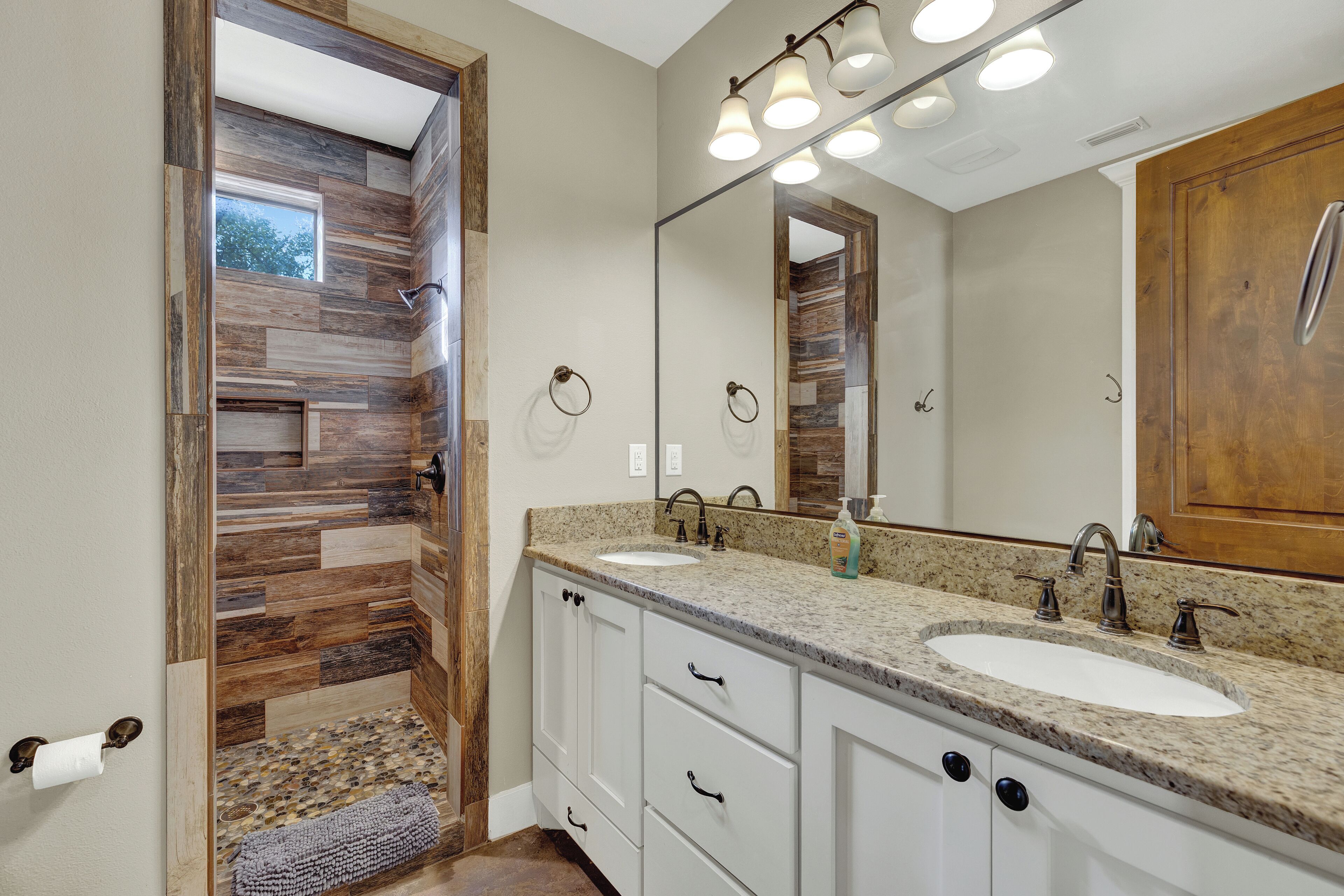 Un baño con pared decorativa de madera, un espejo grande y tocador doble.