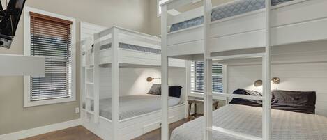 A room with bunk beds, built-in shelves, and a desk with a lamp.