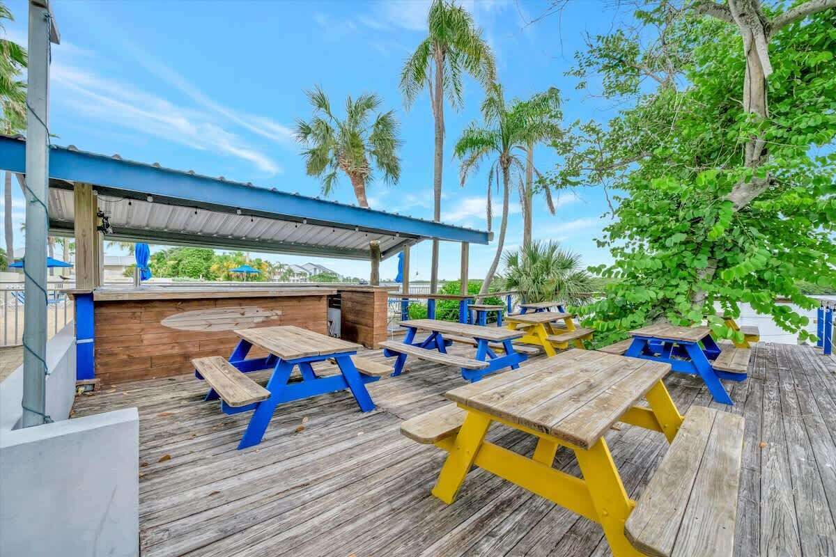 Een terras buiten met houten picknicktafels en een overdekte zithoek.