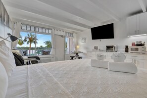 A hotel room with a large bed, a flat-screen TV, a kitchenette, and a balcony with a view of palm trees. - Little Harbor (Ruskin)