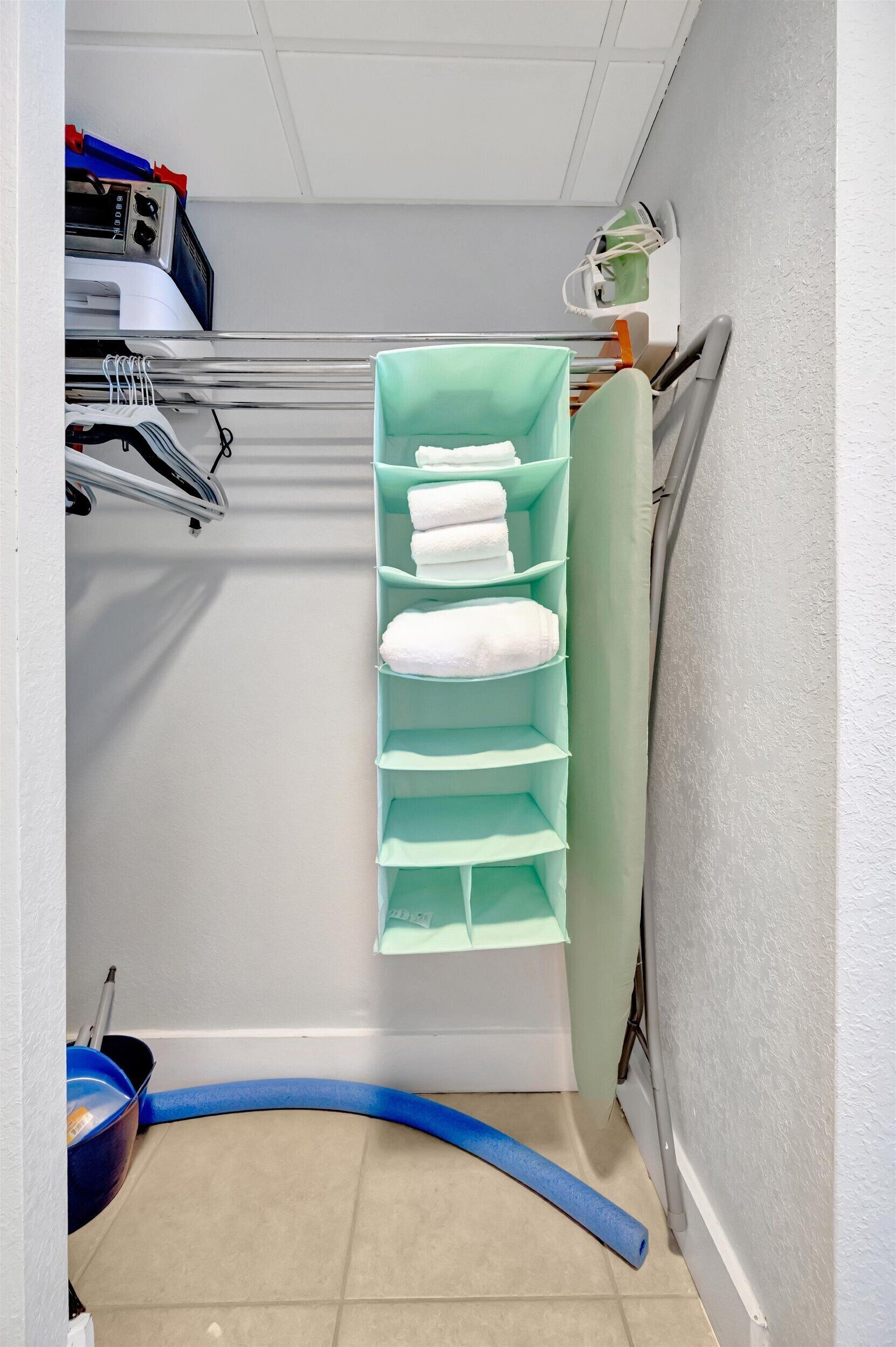 Ein Stauraum mit Regalen für gefaltete Handtücher, einer Wäscheständer und einem blauen Schlauch auf dem Boden.
