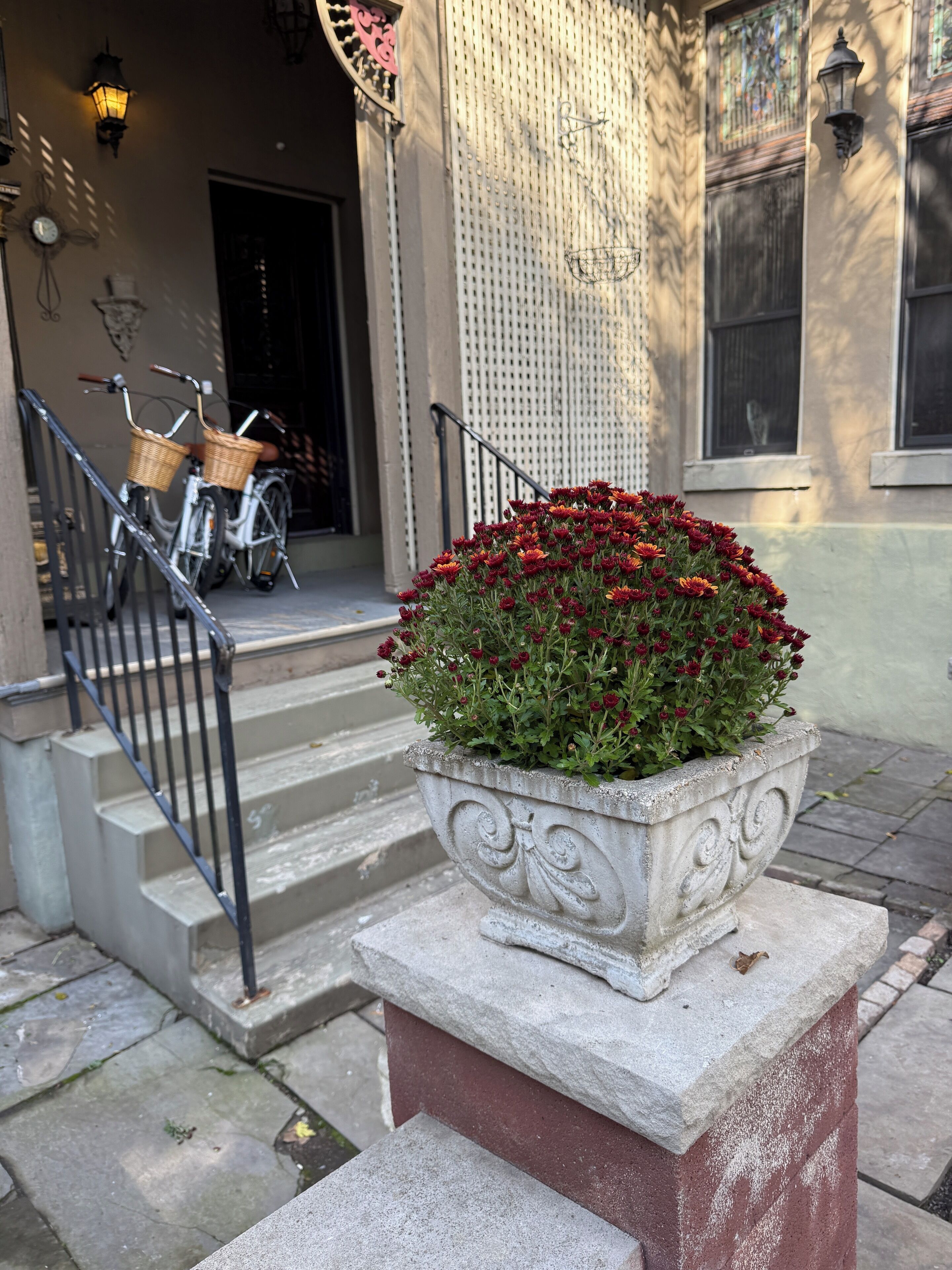 A stone planter with red flowers on a sidewalk, a staircase with a metal railing, and bicycles parked against a building facade.