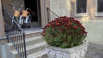 A stone planter with red flowers on a sidewalk, a staircase with a metal railing, and bicycles parked against a building facade.