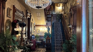 An ornate hallway with a grand chandelier, a staircase, and various decorative items. - The Stegmaier Guest House (Wilkes-Barre)