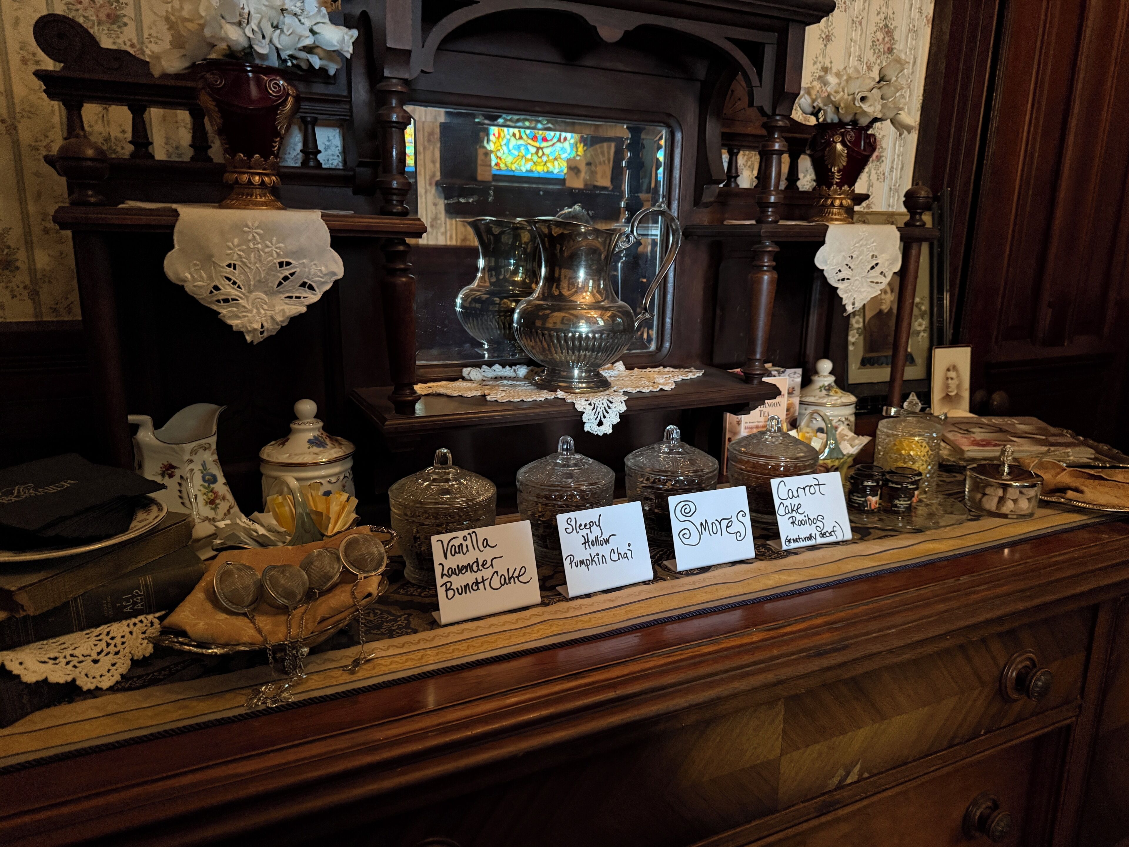 A display of antique kitchenware and jars with labels indicating various contents like 'Vanilla Bundt Cake' and 'Carrot Cake.'