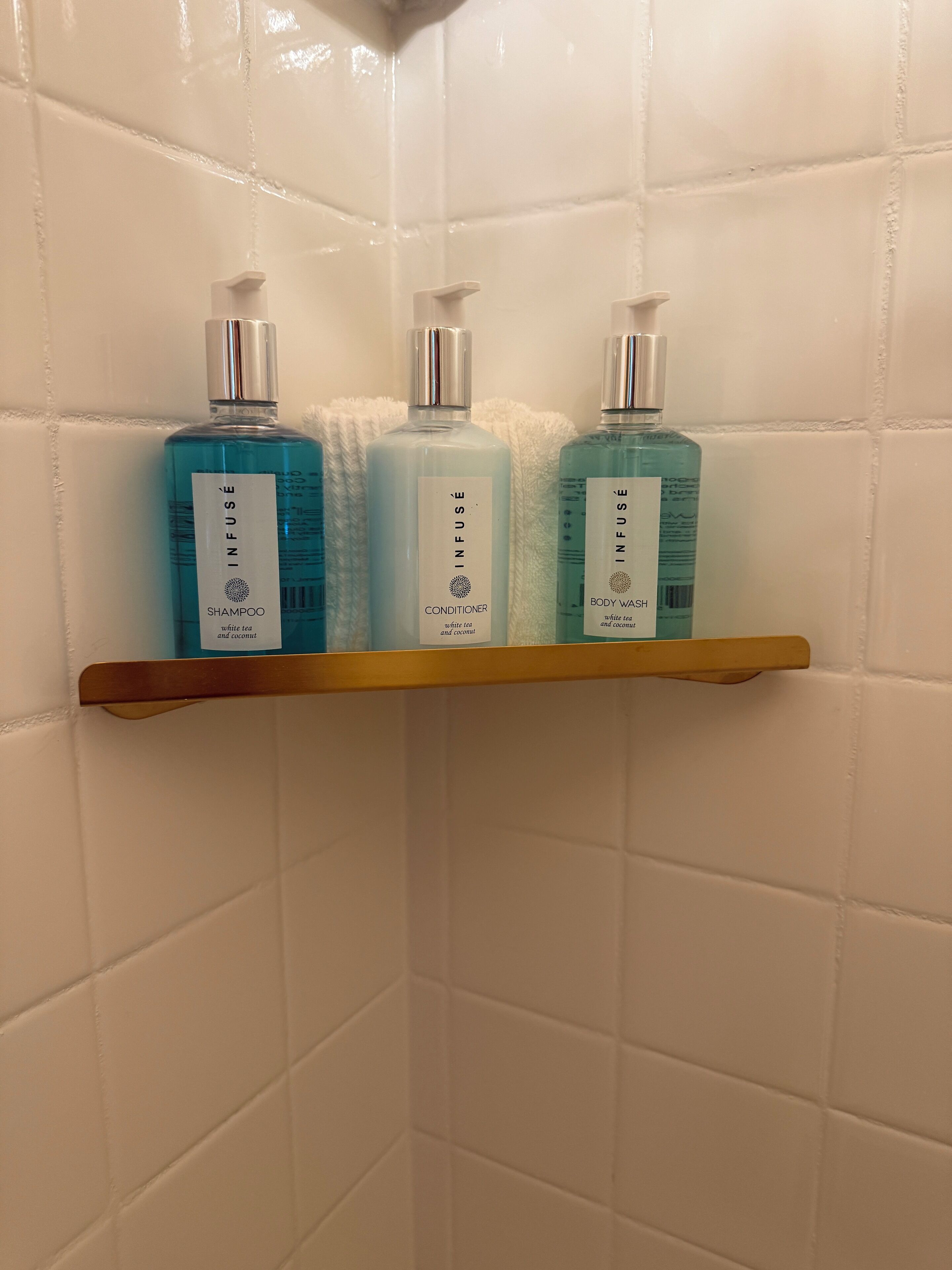 A bathroom shelf with three bottles of Infuse products: shampoo, conditioner, and body wash.