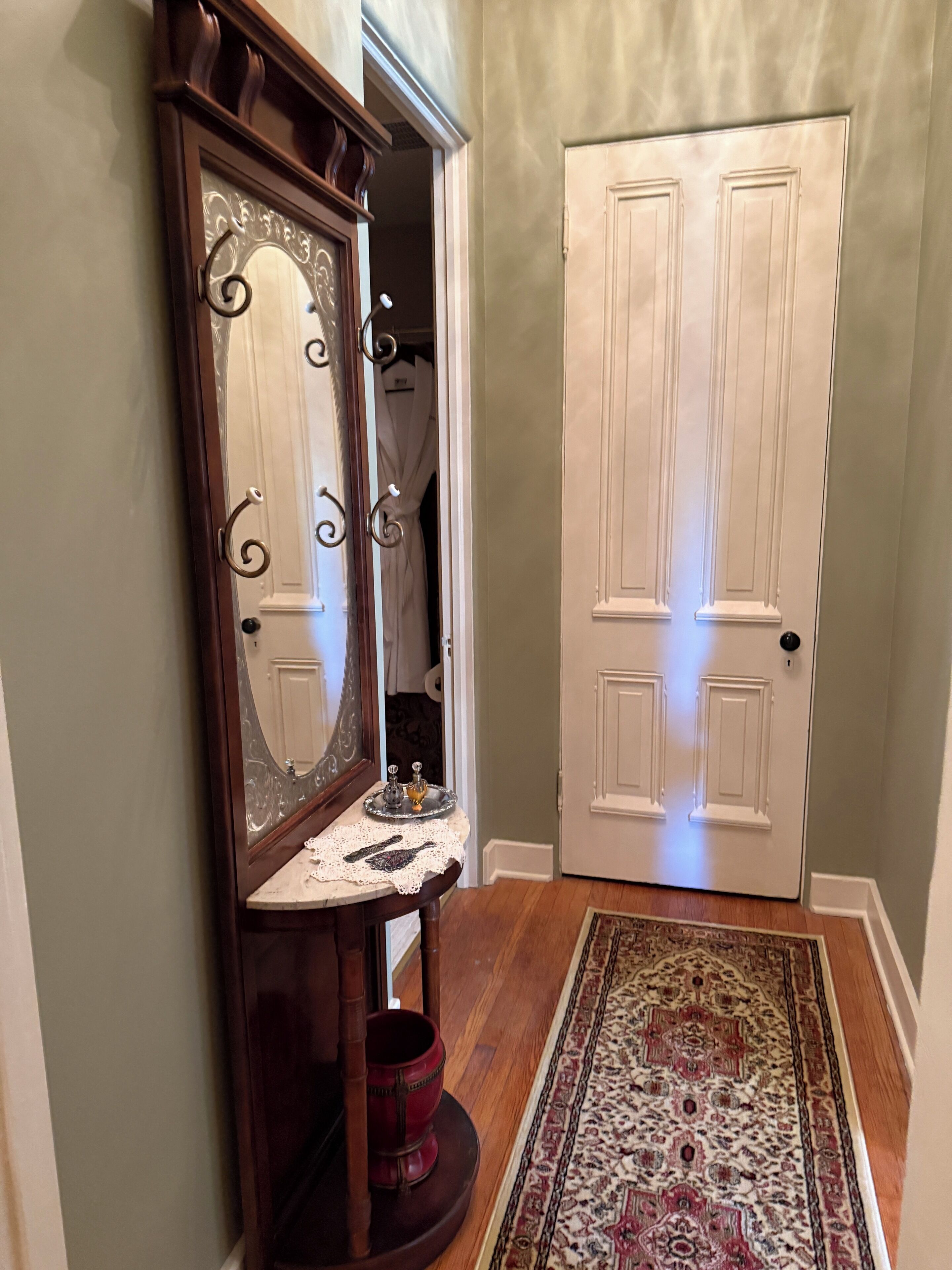 A hallway with a wooden console table, a mirror, a red pot, and a patterned rug.