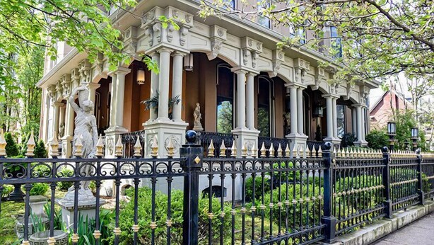 A classical building with ornate columns and statues, surrounded by a black wrought iron fence and lush greenery. - The Stegmaier Guest House (Wilkes-Barre)