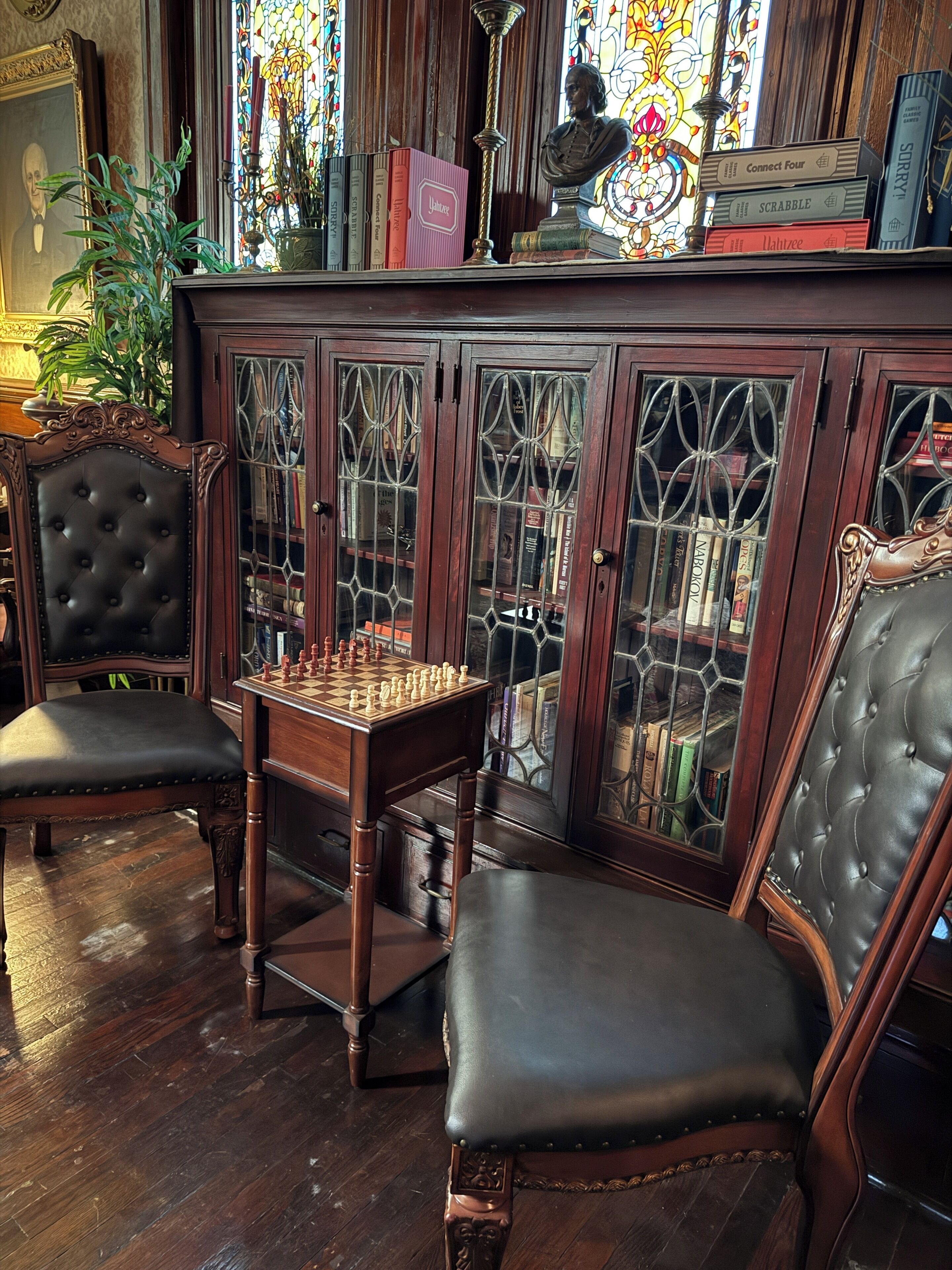 A chessboard set on a table in front of a bookcase with glass doors.