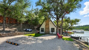 A house with a stone chimney, a gravel driveway, and a red chair near a lake. - The Peaceful Paddle- with dock! (Graford)