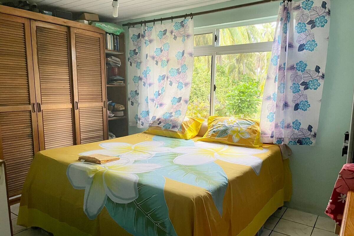 A bedroom with a bed covered in a floral bedspread, a wardrobe, and curtains with a floral pattern.