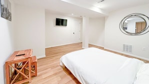 A bedroom with a bed, a wooden side table, a mirror, and a television on the wall.