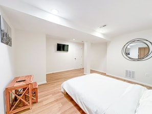Un dormitorio con una cama, una mesita de noche de madera, un espejo y un televisor en la pared.