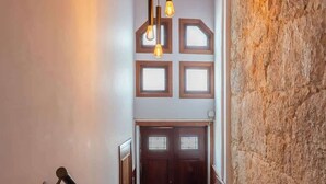 A staircase with a wooden handrail, a wall with a textured stone surface, and a door with a window at the top. - Bright & Spacious Flat in Porto by HostWise (Porto)