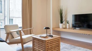 A modern living room with a sofa, a side table with a lamp, a TV on a shelf, and a view of buildings outside. - Modern & Stylish Flat by HostWise (Porto)