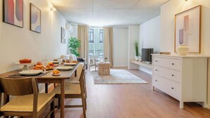A modern dining area with a wooden table set for a meal, a white cabinet, and a television on a stand. - Modern & Stylish Flat by HostWise (Porto)
