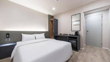 A hotel room with a large bed, a desk with a computer, a mirror, and a wardrobe.