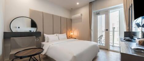 A modern hotel room with a large bed, a round mirror, a desk with a computer, and a view of the city through the window.