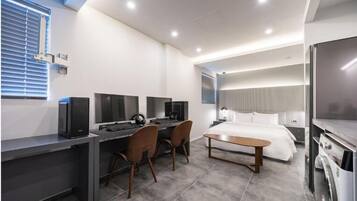Ein modernes Hotelzimmer mit Schreibtisch, zwei Stühlen, einem Bett und einem Fernseher.