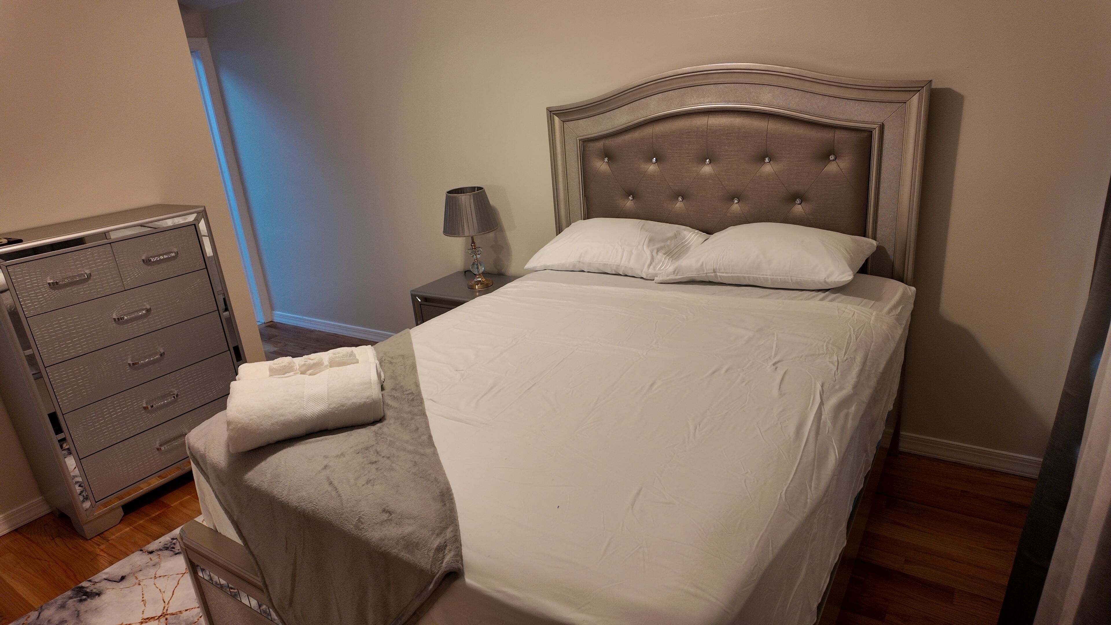 Un lit bien fait, doté d’une tête de lit capitonnée, d’une lampe de chevet et d’un classeur métallique.