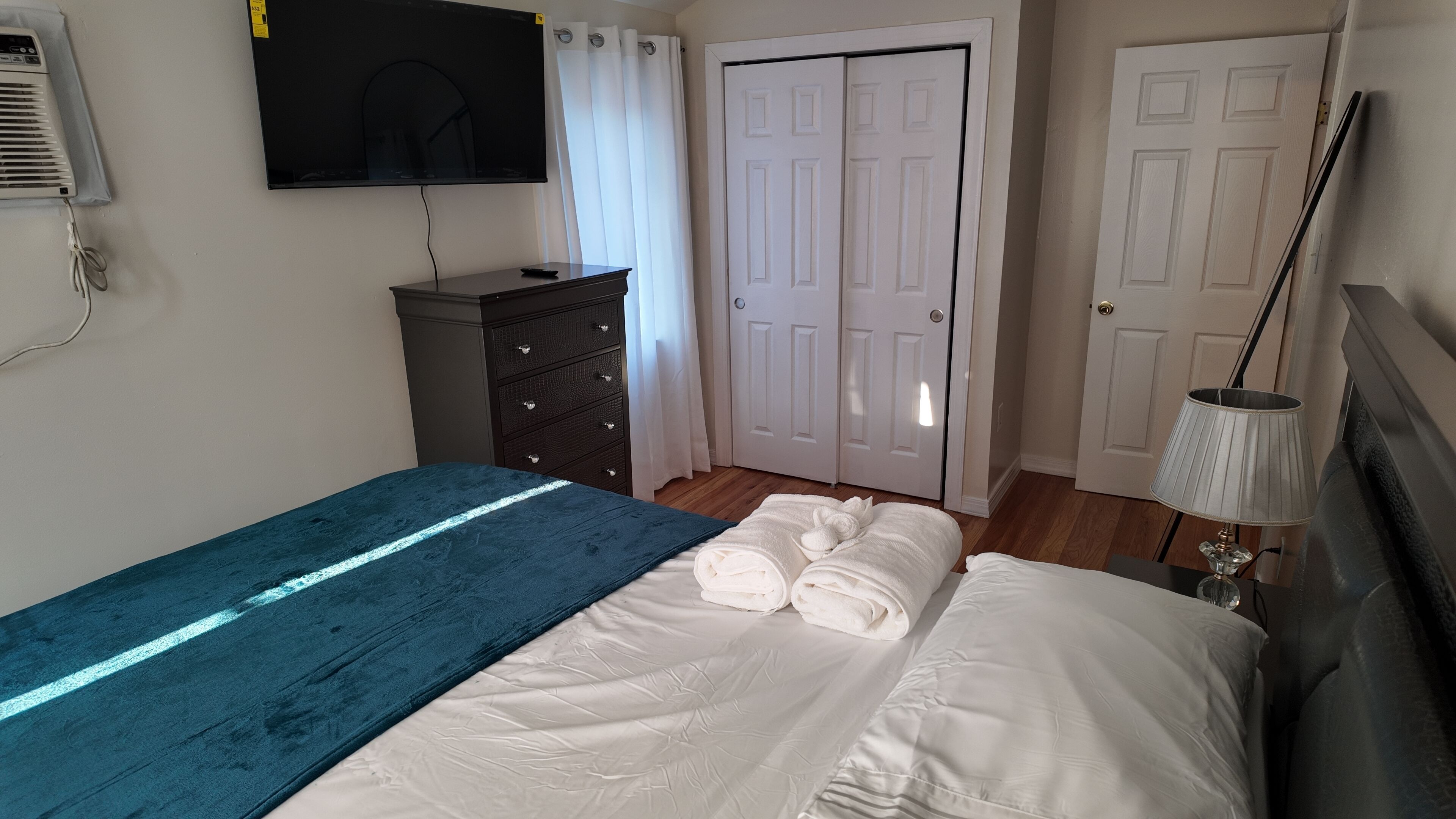 Een slaapkamer met een bed, een dressoir, een televisie en een deur.