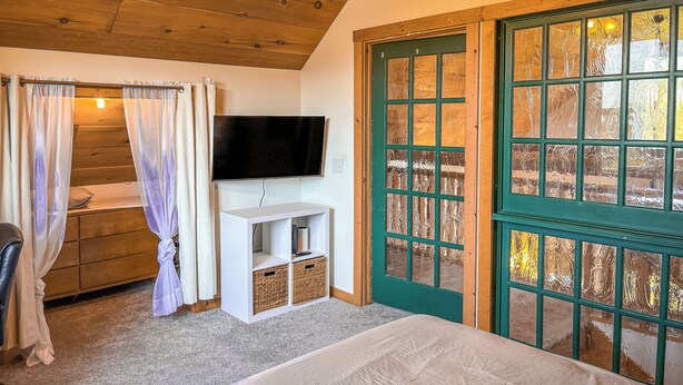 A bedroom with a bed, a TV, a wooden ceiling, a green door, and a window. - Tranquility Heights: Deck, 3.5 acres, Darts, Movie Room, Desk w/Printer (Ozark)