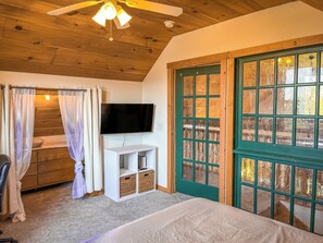 A bedroom with a bed, a TV, a wooden ceiling, a green door, and a window. - Tranquility Heights: Deck, 3.5 acres, Darts, Movie Room, Desk w/Printer (Ozark)