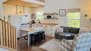 A modern kitchen with wooden accents, a dining area with stools, and a cozy seating area with a couch and armchairs. - Tranquility Heights: Deck, 3.5 acres, Darts, Movie Room, Desk w/Printer (Ozark)